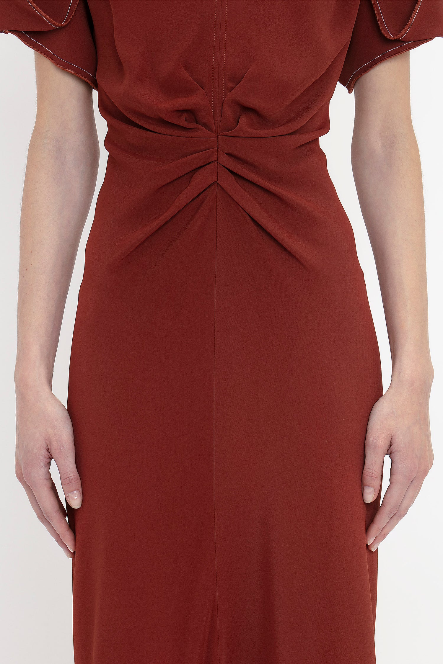 A person wearing a Gathered V-Neck Midi Dress In Russet by Victoria Beckham, featuring waist-defining pleat detail, with both arms hanging straight down by their sides.
