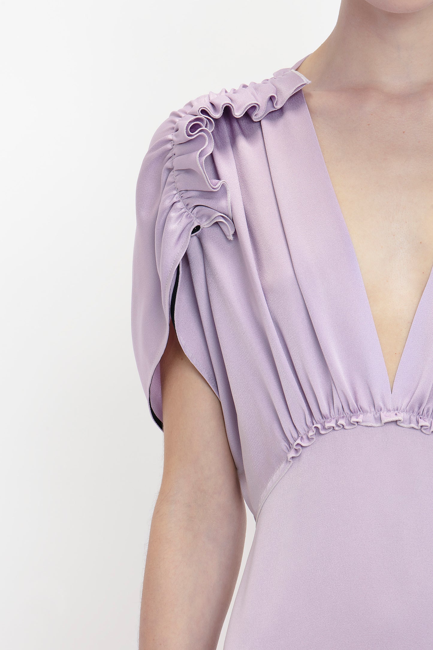 Close-up of a person wearing an elegant Victoria Beckham V-Neck Ruffle Midi Dress In Petunia with ruffled shoulder details reminiscent of Victoria Beckham's sophisticated style. The background is plain white.