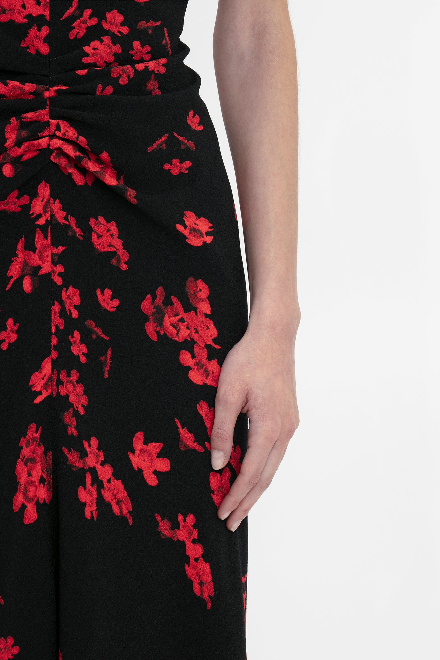 A person wearing a Victoria Beckham Gathered Waist Midi Dress In Sci-Fi Black Floral with red floral patterns and a fit-and-flare silhouette; their right hand rests at their side.