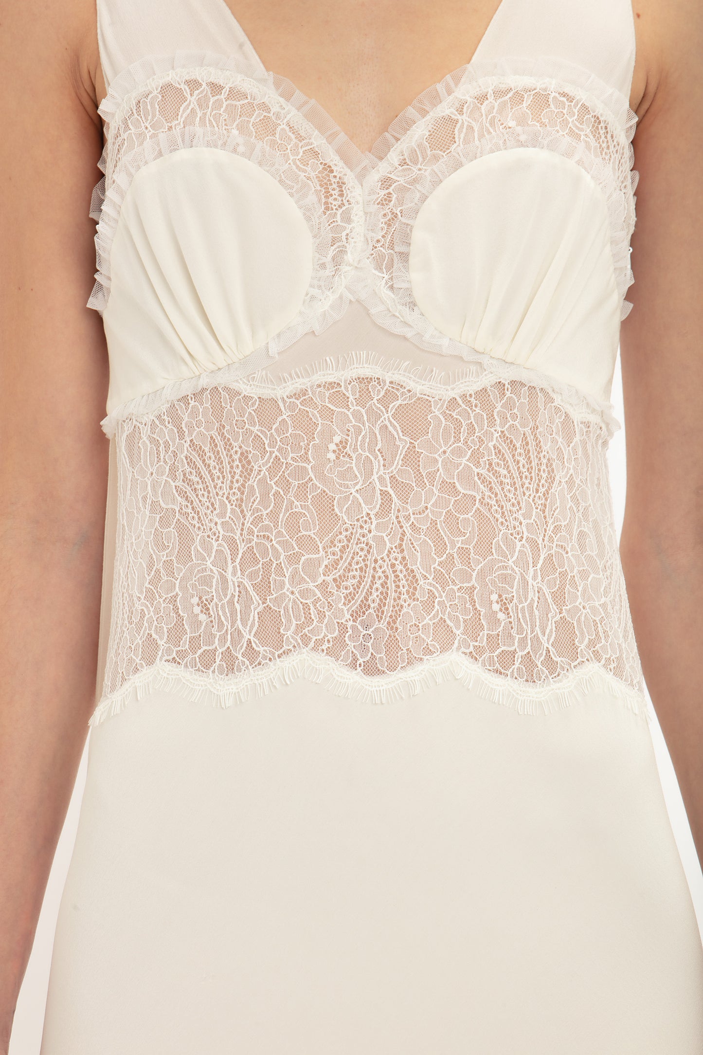 Close-up of a person wearing the Ruffle Detail Midi Dress In Ivory by Victoria Beckham, which features sheer, tactile lace detailing on the bodice and straps. The lace features a floral pattern.