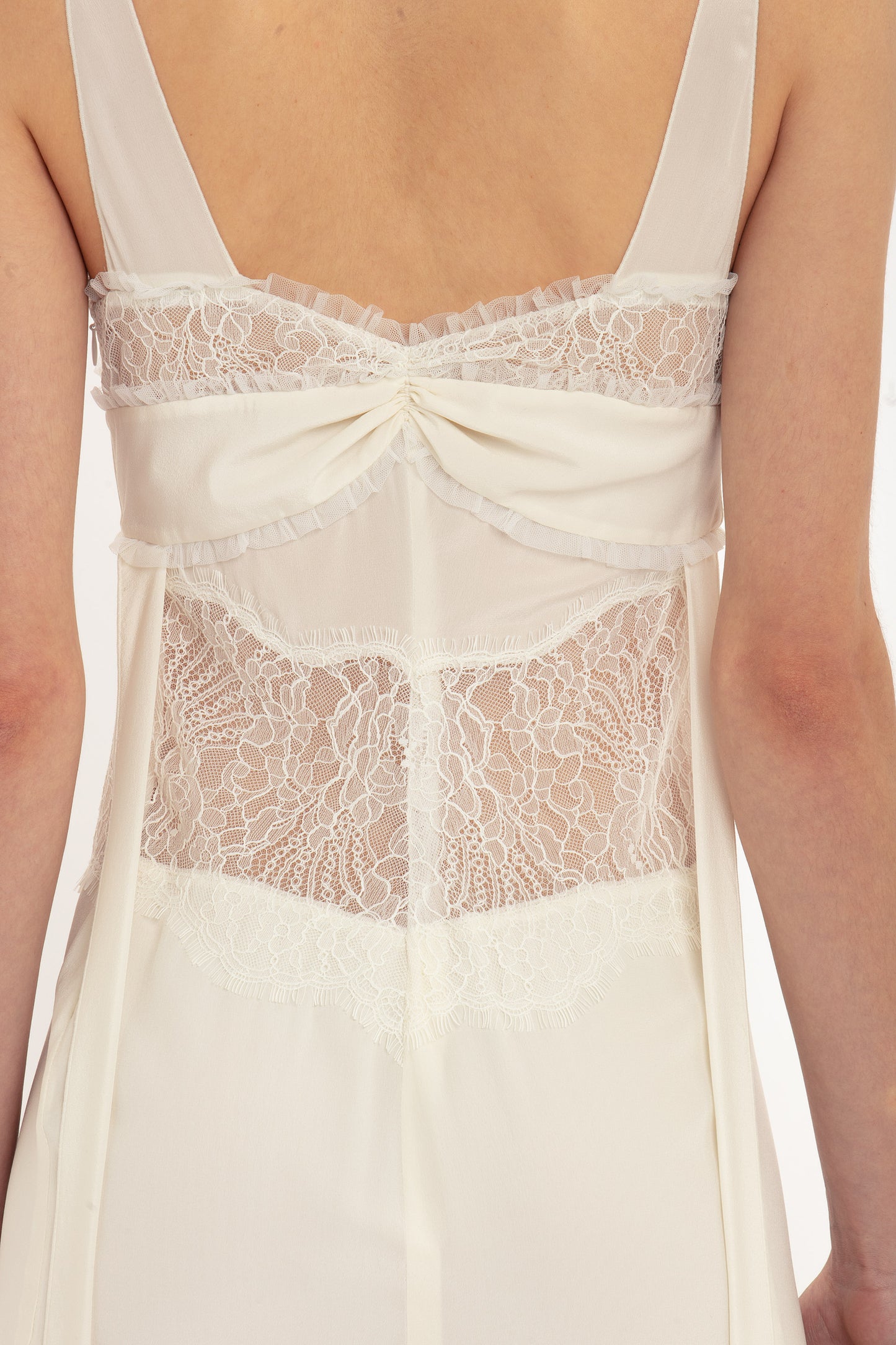 Back view of a person wearing a Victoria Beckham Ruffle Detail Midi Dress In Ivory, showing intricate tactile lace detailing and pleats on the upper and middle sections.