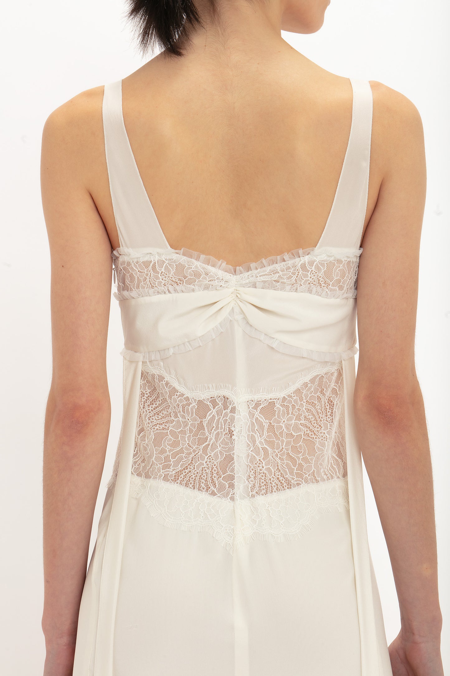 A person is shown from the back in a Ruffle Detail Midi Dress In Ivory by Victoria Beckham, highlighting the intricate tactile lace and fabric details.