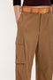 Close-up of a person wearing Victoria Beckham Relaxed Cargo Trouser In Tobacco with a large side pocket, brown belt, and a dark long-sleeve top. The military-inspired style is emphasized by the practical design. The background is plain white.