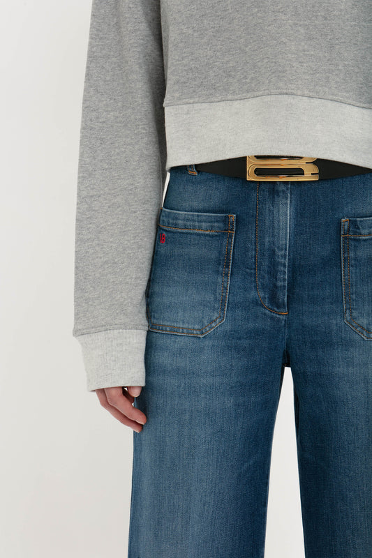 Close-up of a person wearing blue jeans and a grey marl sweater, with a hand in their pocket, showing a belt and partial Victoria Beckham logo on their Cropped Sweatshirt In Grey Marl.