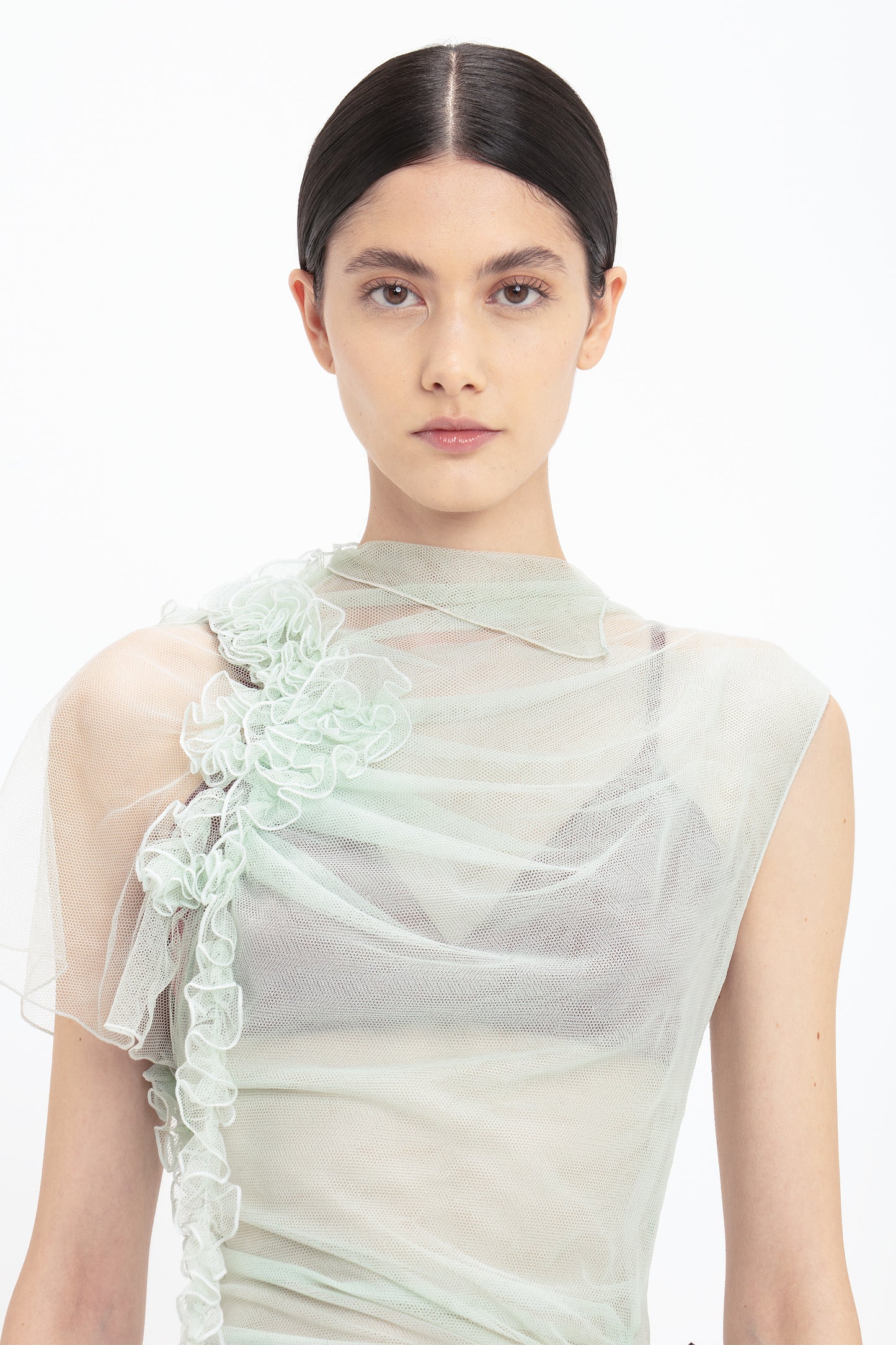 Person with dark hair styled in a center part wearing a Gathered Tulle Detail Floor-Length Dress In Jade by Victoria Beckham, looking directly at the camera.