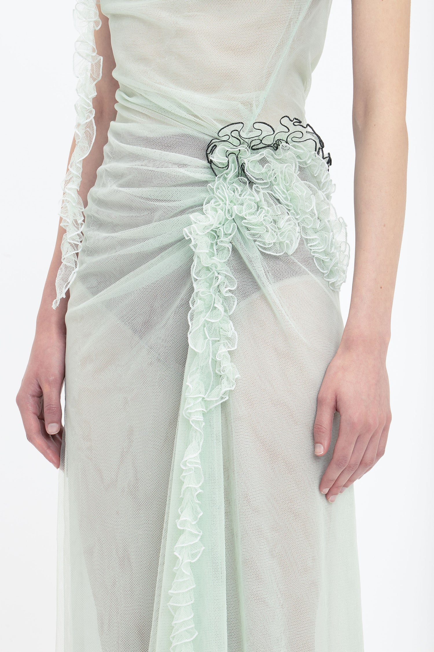 Close-up of a person wearing the Victoria Beckham Gathered Tulle Detail Floor-Length Dress In Jade with intricate floral ruche detailing and a decorative black element at the waist.