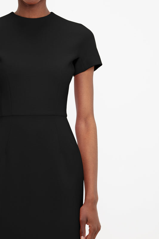 A close-up of a woman in a Victoria Beckham fitted T-shirt dress in black, focusing on the upper torso and arm without showing the head.