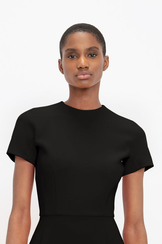 Portrait of a woman with short hair wearing a Victoria Beckham Fitted T-Shirt Dress In Black, facing the camera with a neutral expression on a white background.
