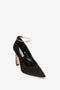 A Pointy Toe Pump in Black Satin by Victoria Beckham with a 100mm heel, featuring a pointed toe and a thin ankle strap adorned with a gold clasp. The shoe boasts a beige sole and a zipper at the heel, while the ankle strap resembles an elegant metal bracelet.