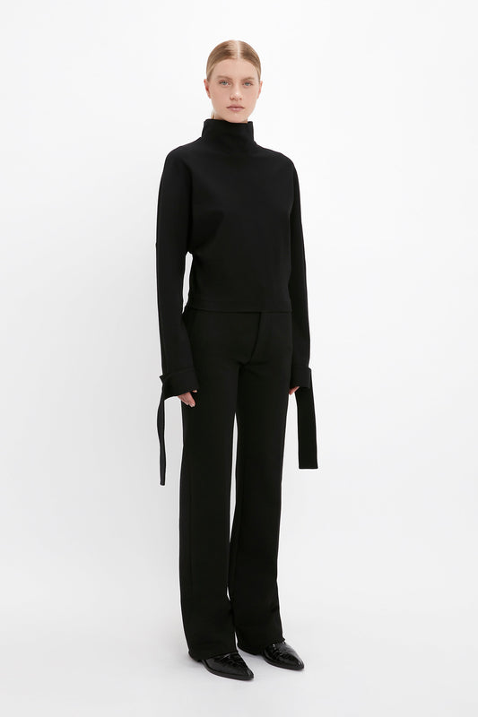Person wearing a black Victoria Beckham Tie Sleeve Ponti Top In Black with an oversized slouchy fit and wide-leg pants stands against a plain white background.