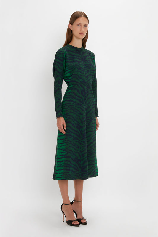 Woman in a long-sleeved green and black tiger stripe Victoria Beckham Dolman Midi Dress standing against a white background. She wears black Pointy Toe Stiletto Sandals.