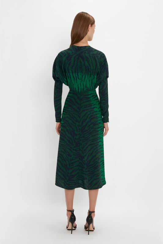 Woman from behind wearing a Victoria Beckham Dolman Midi Dress In Green-Navy Tiger Print and black pointy toe stiletto sandals, standing against a plain white background.