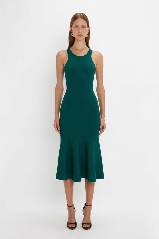 Woman wearing the VB Body Sleeveless Dress In Lurex Green by Victoria Beckham in a fitted, dark green fabric with a flared silhouette, perfect for updating your new-season wardrobe, standing straight against a plain white background.