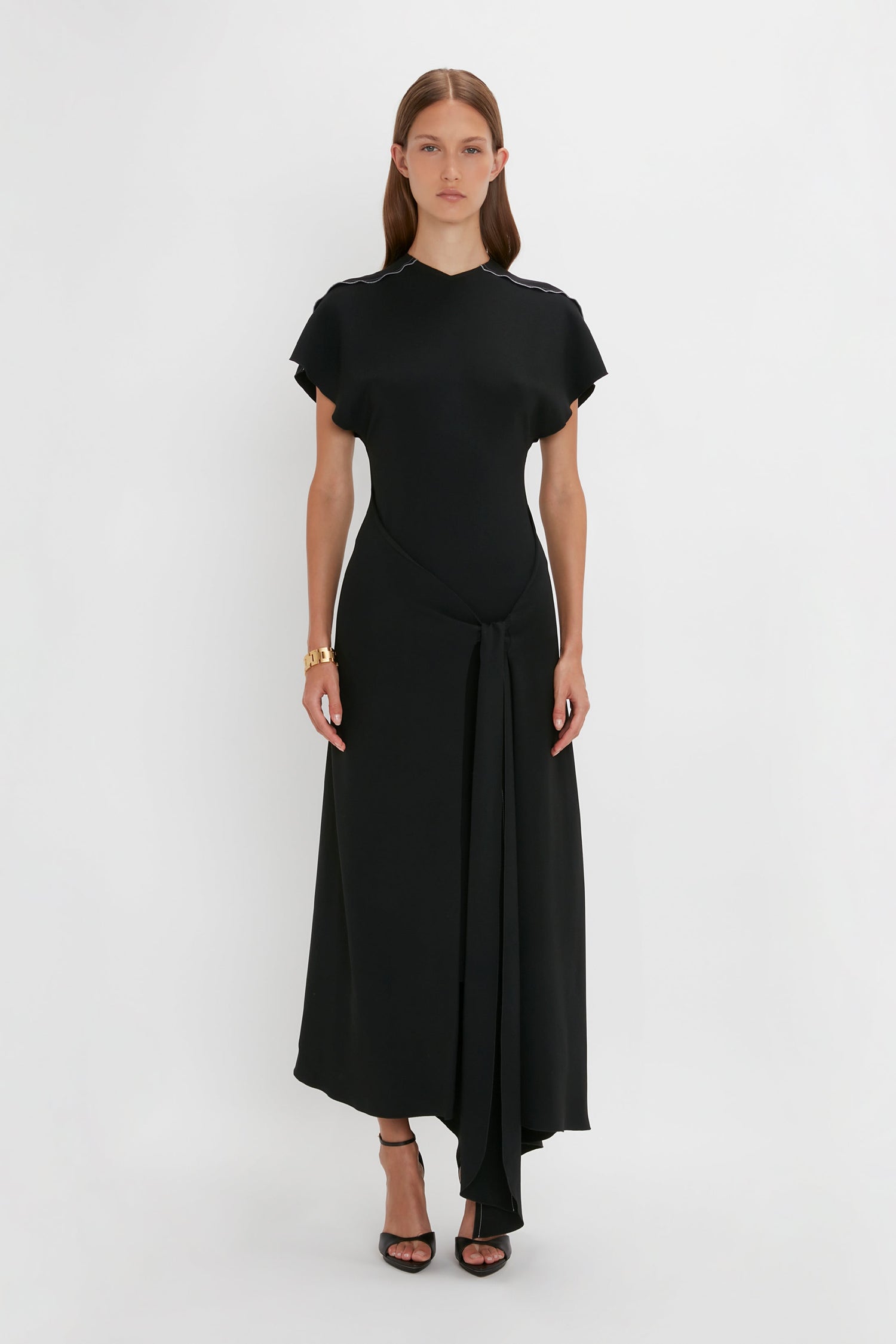 A woman wearing a sophisticated crew-neck black Short Sleeve Tie Detail Dress In Black by Victoria Beckham, standing against a plain white background.