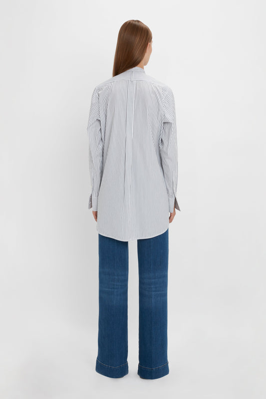 Person with long hair wearing a Victoria Beckham Tuxedo Bib Shirt in Black and Off-White and wide-legged blue jeans, crafted from organic cotton, standing with their back to the camera against a plain white background.