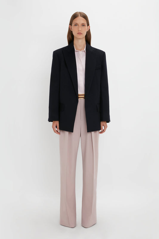 A person stands against a plain white background wearing a Peak Lapel Jacket In Midnight over a light-colored shirt with light pink pants, evoking a contemporary feel. They face forward with a neutral expression, capturing the essence of Victoria Beckham's sophisticated style.
