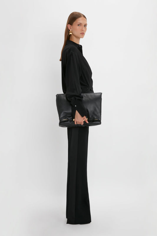 A woman stands against a white background, dressed in modern evening wear, holding a Satin Panel Straight Leg Trouser by Victoria Beckham.