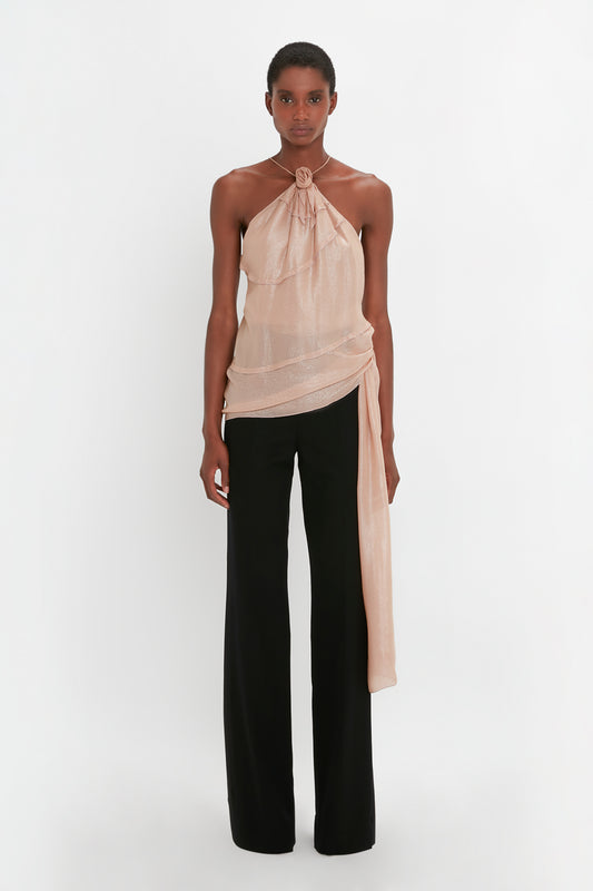 A person stands against a white background wearing a sleeveless Flower Detail Cami Top In Rosewater by Victoria Beckham and black Satin Panel Straight Leg Trousers.
