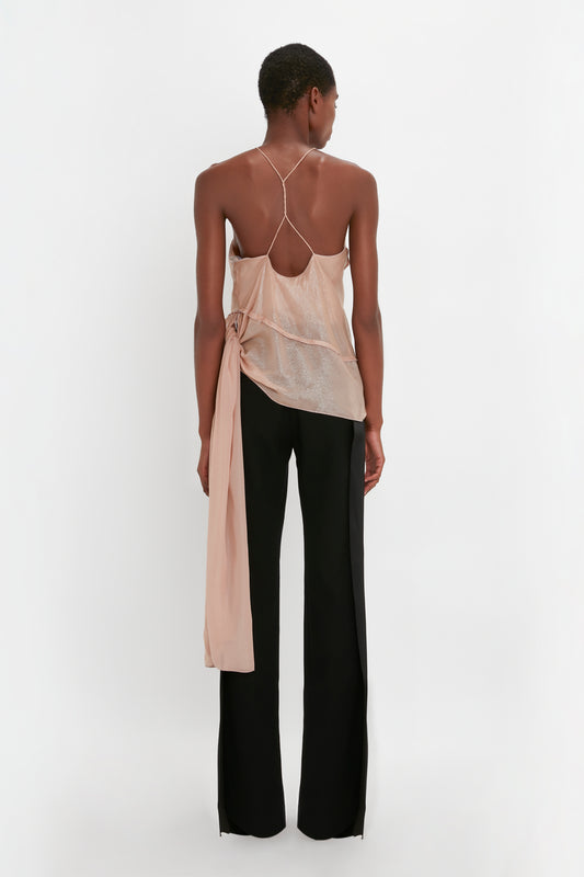 Person standing with back facing the camera, wearing a Victoria Beckham Flower Detail Cami Top In Rosewater and black Satin Panel Straight Leg Trousers against a plain white background.