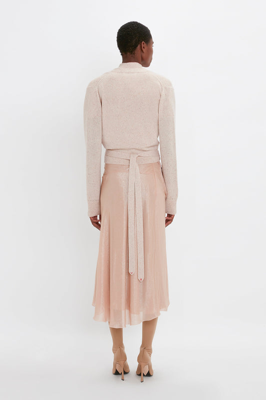 Person standing with their back to the camera, wearing a light pink long-sleeved top, a matching Victoria Beckham Flower Detail Cami Skirt In Rosewater with a fit-and-flare silhouette, and beige high-heeled shoes.