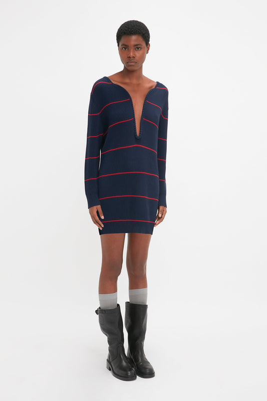 Person stands against a plain white background, wearing the Frame Detail Jumper Dress In Navy-Red by Victoria Beckham, gray knee-high socks, and black boots. The directional curved neckline gives a nod to the latest SS24 runway trends.