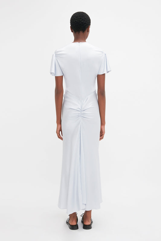 Person standing facing away from the camera, wearing the Victoria Beckham Gathered Sleeve Midi Dress In Ice, featuring short sleeves and a ruched detail at the lower back.