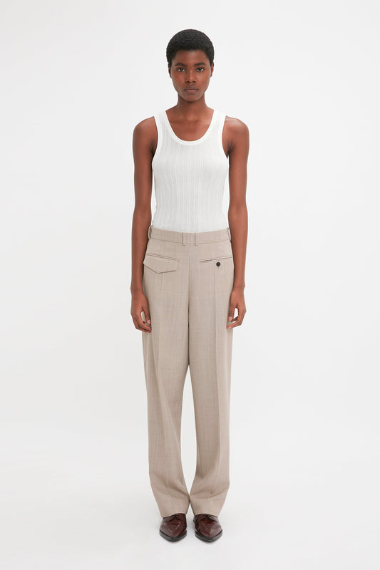 A person stands facing forward against a plain white background, wearing a Fine Knit Vertical Stripe Tank In White by Victoria Beckham, beige pants, and brown shoes.