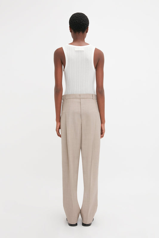 Person standing, facing away, wearing a Fine Knit Vertical Stripe Tank In White and beige trousers against a plain white background. The ensemble, reminiscent of Victoria Beckham's minimalist style, boasts a subtly textured appearance that adds depth to the simplicity.