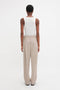 Person standing, facing away, wearing a Fine Knit Vertical Stripe Tank In White and beige trousers against a plain white background. The ensemble, reminiscent of Victoria Beckham's minimalist style, boasts a subtly textured appearance that adds depth to the simplicity.