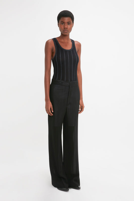 Person standing against a white background, wearing a Fine Knit Vertical Stripe Tank In Black-Blue by Victoria Beckham and black wide-leg pants, with a neutral expression.