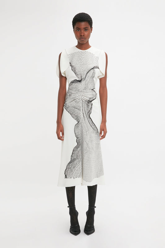 A young black woman standing straight and facing the camera, wearing a Victoria Beckham Gathered Waist Midi Dress In White-Black Contorted Net with abstract print.