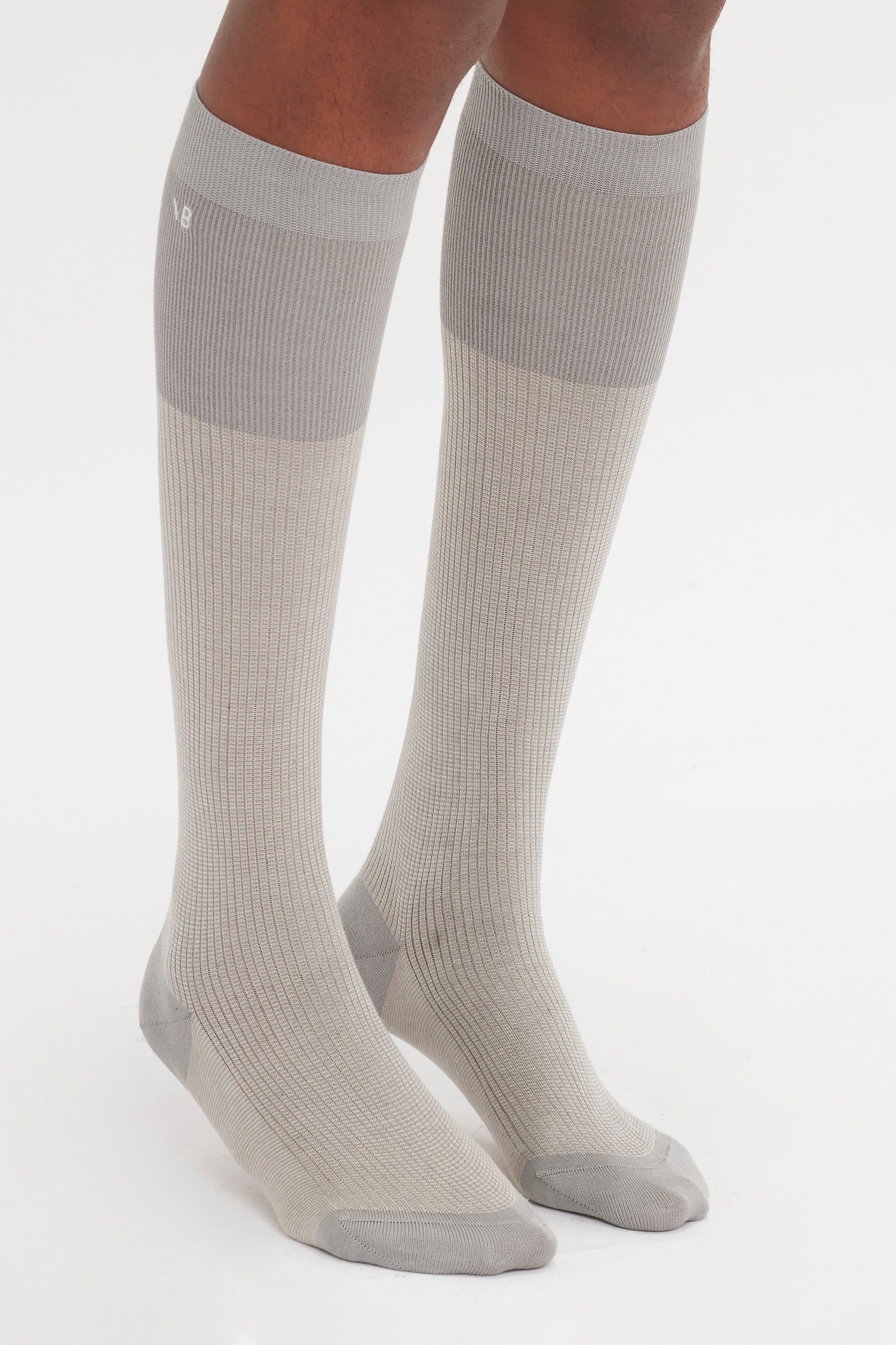 A person wearing a pair of Victoria Beckham Superfine Rib Socks In Lunar Grey and Sesame knee-high socks with a superfine ribbed design.