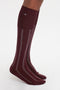 A pair of feet wearing Victoria Beckham Superfine Rib Socks In Burgundy, made from 100% cotton superfine ribbed fabric, against a white background.