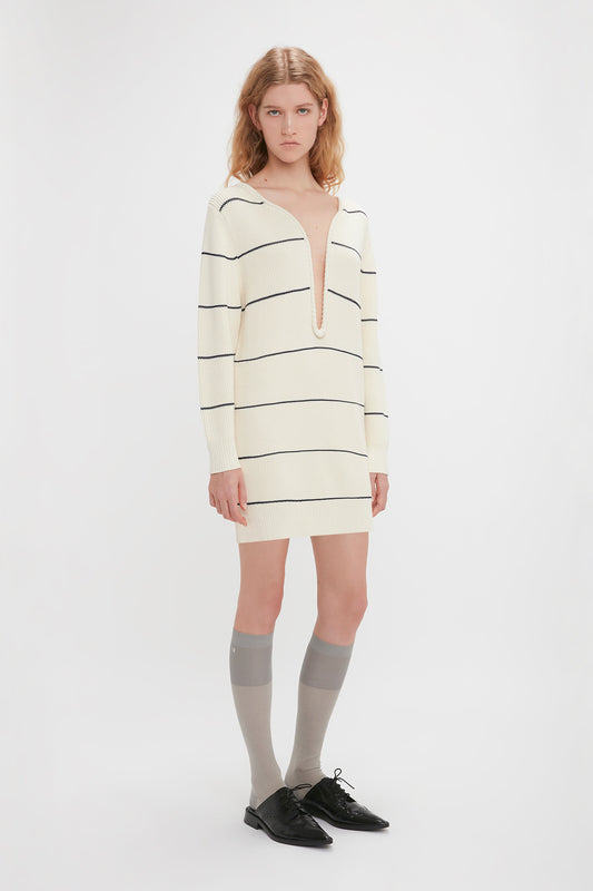 A person stands against a white background wearing the Victoria Beckham Frame Detail Jumper Dress In Natural-Navy. They complete the look with knee-high gray socks and black shoes.
