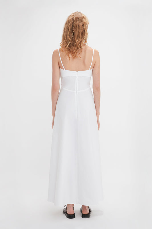 A person with curly blonde hair in a sleeveless white Cami Fit And Flare Midi In White by Victoria Beckham is standing with their back facing the camera against a plain white background.