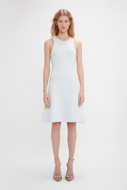 A woman wearing a sleeveless white, body-sculpting Victoria Beckham Sleeveless Tank Dress In Ice and high heels stands facing the camera against a plain white background.
