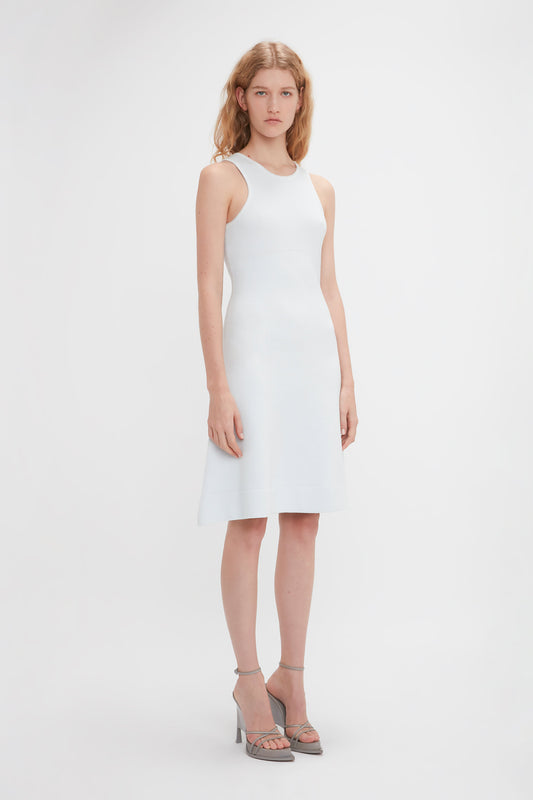 A woman with long blonde hair is standing and wearing a Sleeveless Tank Dress In Ice by Victoria Beckham paired with high-heeled sandals. She is looking directly at the camera against a plain white background.