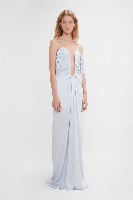 Person wearing a light blue Frame Detail Cut-Out Cami Dress In Ice by Victoria Beckham in crepe back satin with thin shoulder straps and a deep V neckline, standing against a plain white background. Perfect eveningwear choice.