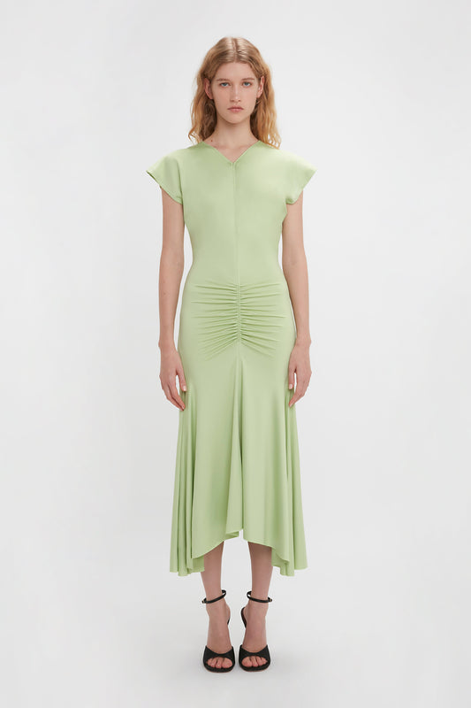 A woman in a pale pistachio, Victoria Beckham Sleeveless Ruched Jersey Dress with cap sleeves and ruched detailing, standing against a white background.