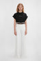 Young woman wearing a Victoria Beckham 'Do As I Say, Not As I Do' Slogan T-shirt in black and white high-waisted flared jeans, standing against a plain white background.