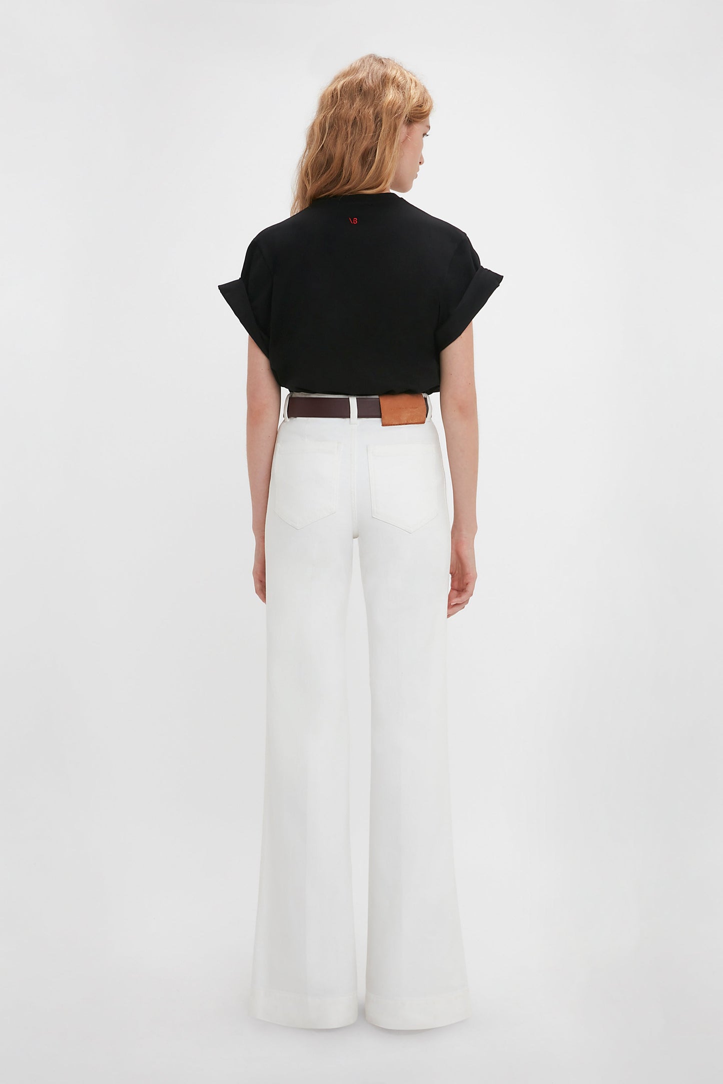 Woman seen from behind wearing a Victoria Beckham 'Do As I Say, Not As I Do' Slogan T-Shirt In Black and white wide-leg trousers with a brown belt against a plain background.