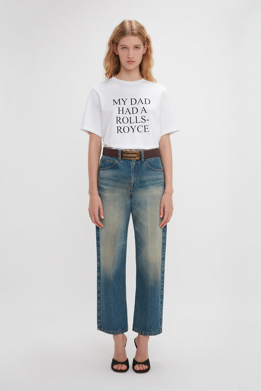 A woman in a Victoria Beckham organic cotton T-shirt that reads "my dad holds a Rolls-Royce" and blue jeans stands against a plain background.