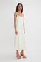 A woman with long hair stands in a sleeveless, ankle-length, off-white camisole dress and tan heels against a plain white background wearing the Exclusive Panelled Midi Cami Dress In Vanilla by Victoria Beckham.