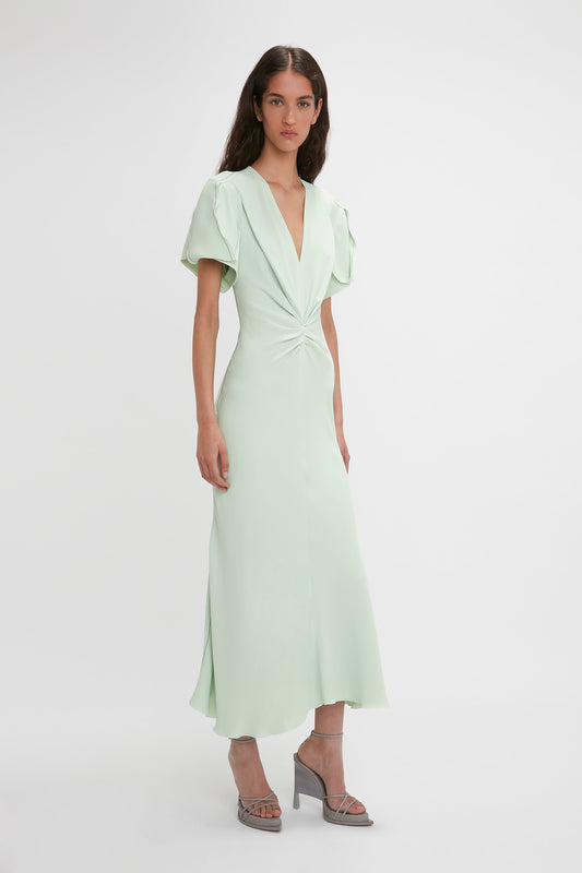 A woman in a Victoria Beckham Gathered V-Neck Midi Dress In Jade, standing against a white background.