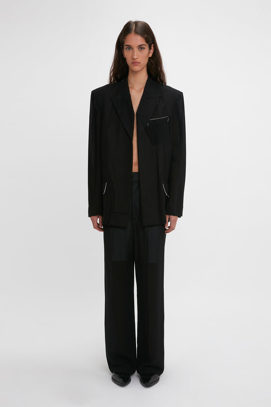 A woman models a Victoria Beckham black pantsuit featuring a Fold Detail Tailored Jacket with an unbuttoned blazer, standing against a plain white background.