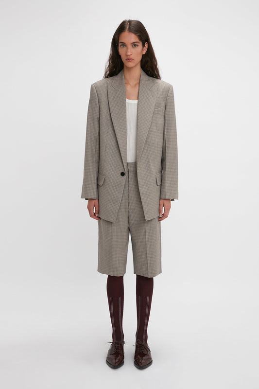 A person stands against a plain background, wearing the Peak Lapel Jacket In Multi by Victoria Beckham, matching long shorts, a white top, maroon knee-high socks, and black shoes.