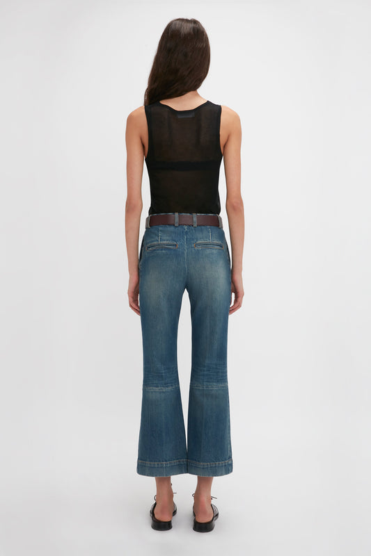 A woman wearing a Victoria Beckham Lightweight Tank Top In Black and blue wide-leg jeans stands facing away from the camera against a plain white background.