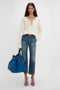 A person wearing a white sweater, blue jeans, and gray heels stands holding a Victoria Beckham W11 Medium Tote Bag In Vibrant Blue against a plain background.