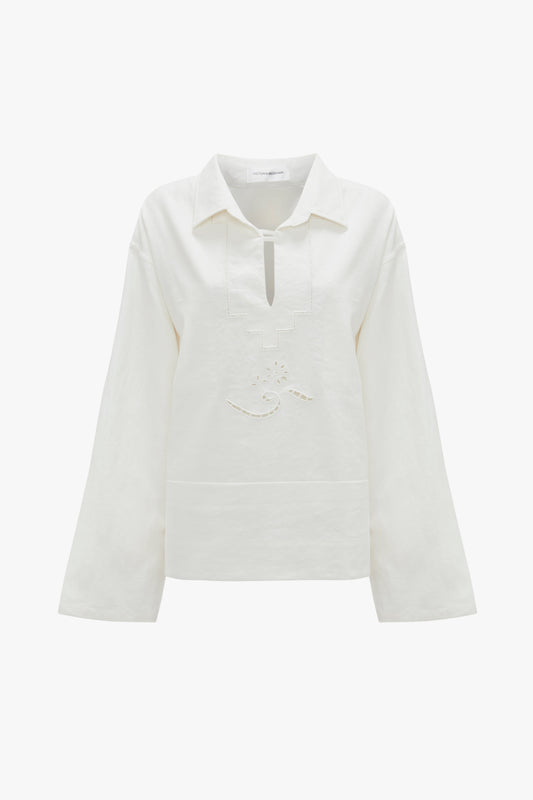 Victoria Beckham's Oversized Embroidered Tunic In Antique White long-sleeve shirt with a collar and a keyhole neckline, crafted from a linen-cotton blend. It features subtle embroidery detailing on the front, reminiscent of Victoria’s runway picks.
