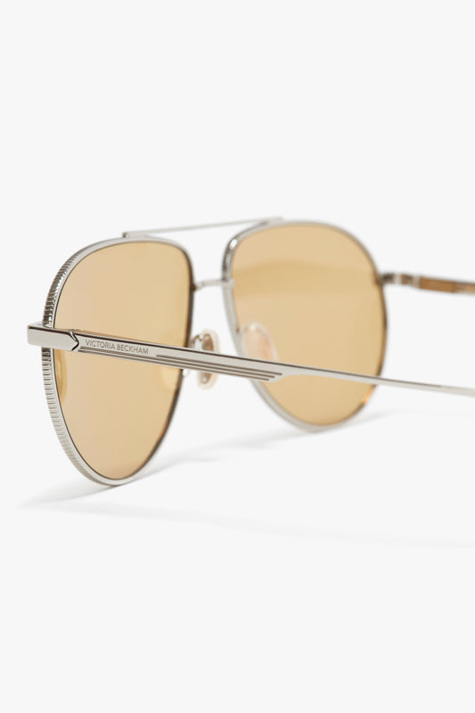 A close-up of Victoria Beckham V Metal Pilot sunglasses in silver-brown with light brown tinted lenses and slim metal frames, on a white background.